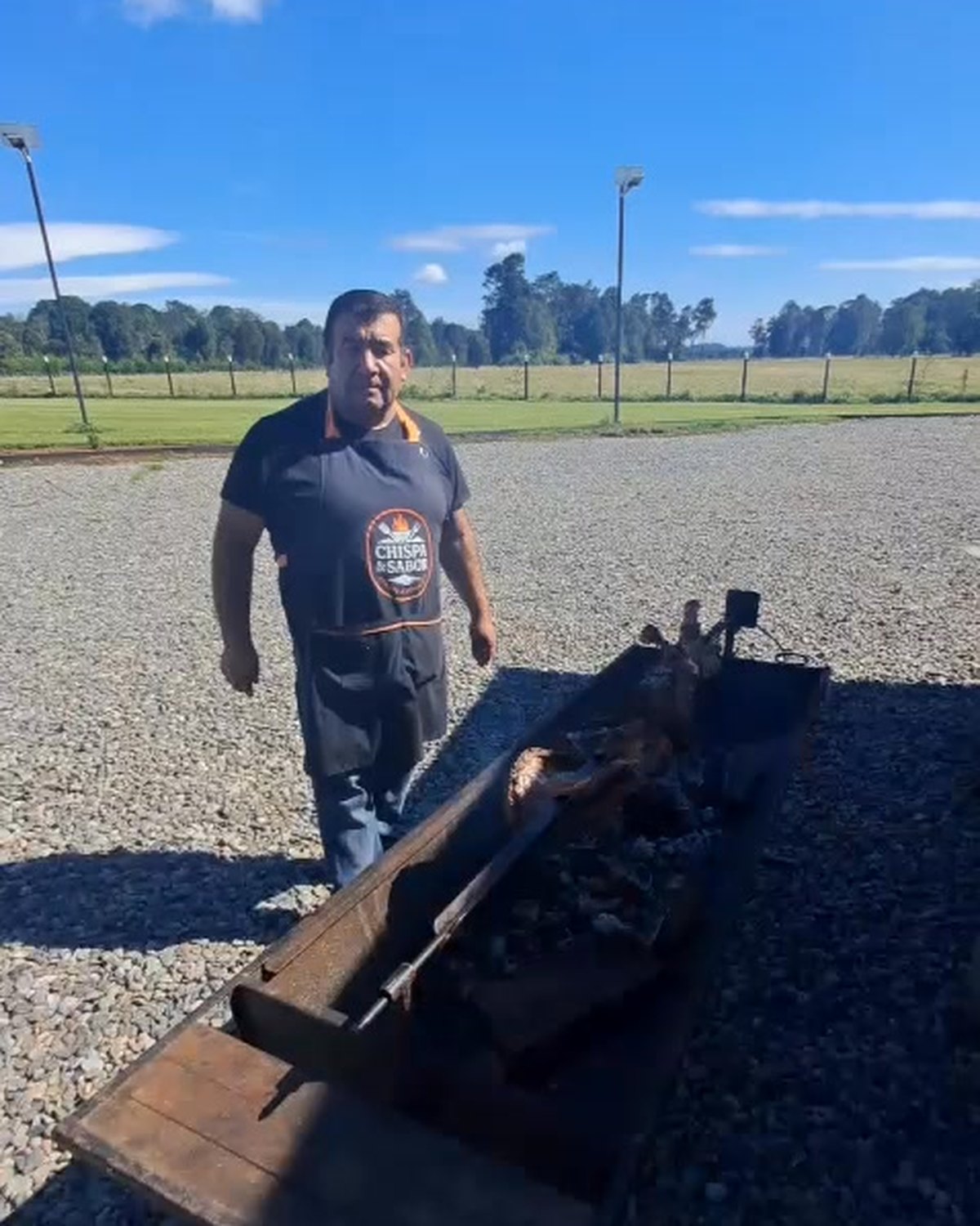 Cordero al palo asándose sobre brasas en una cancha abierta