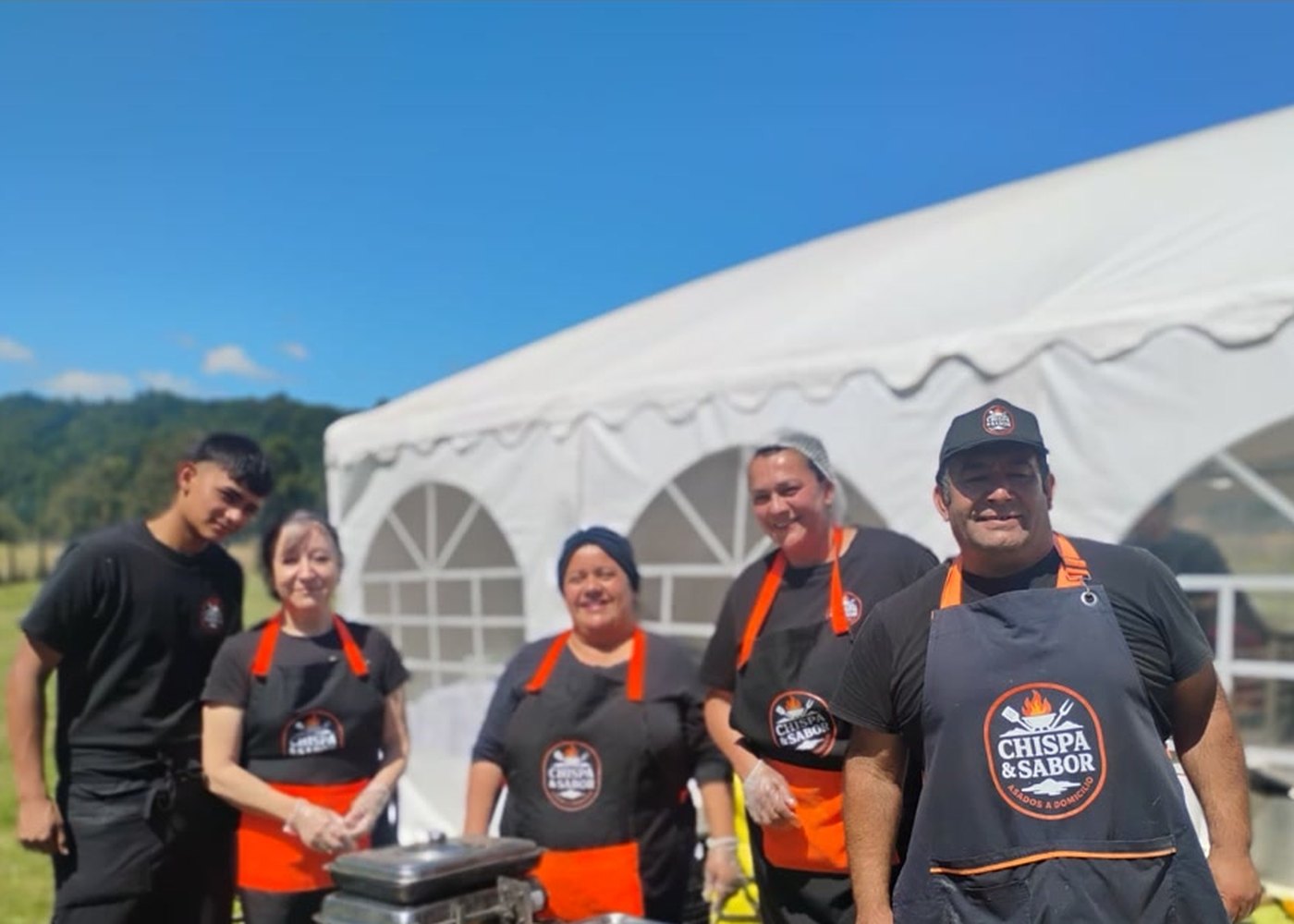Equipo completo de Chispa y Sabor frente a una carpa de evento en un día soleado