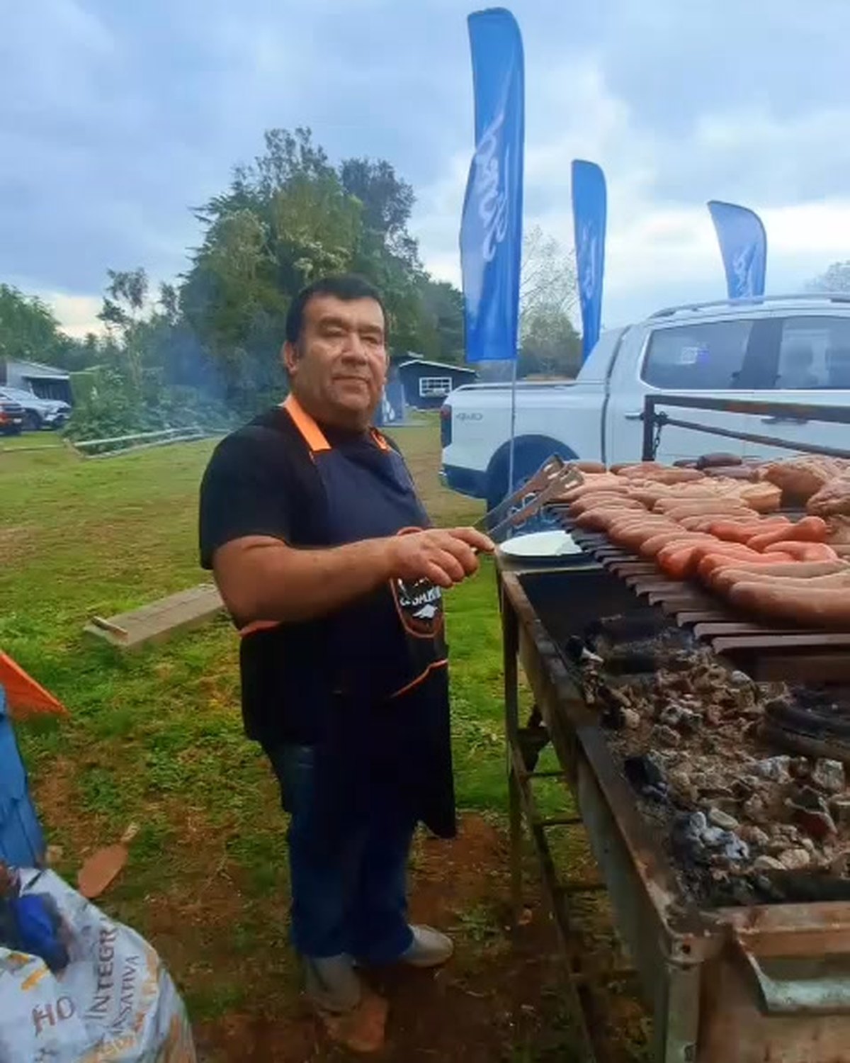 El dueño de Chispa y Sabor atendiendo una parrilla llena de carnes en un evento al aire libre
